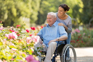 Senior man sitting on a wheelchair with caregiver, walking in a park